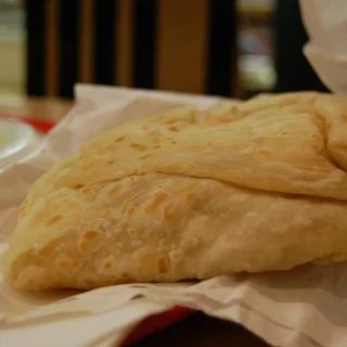 A paratha roti on paper, torn into soft layers