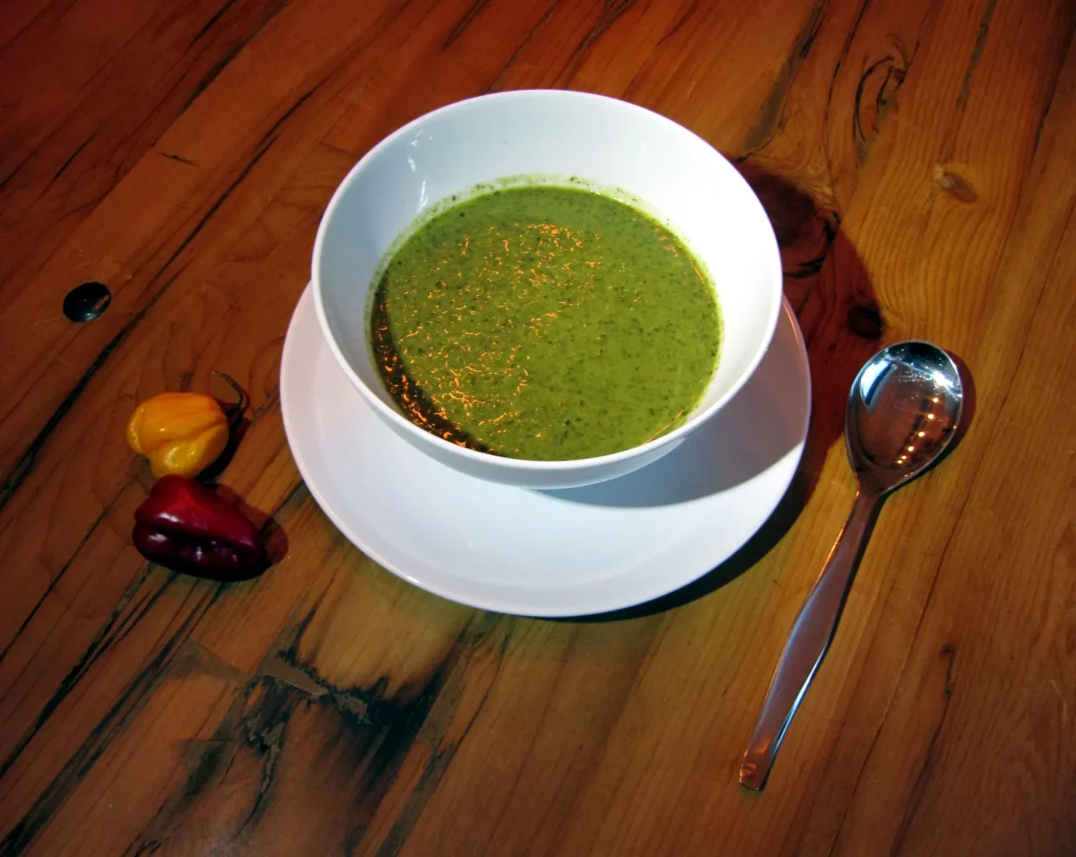 A bowl of smooth green callaloo with hot peppers beside it