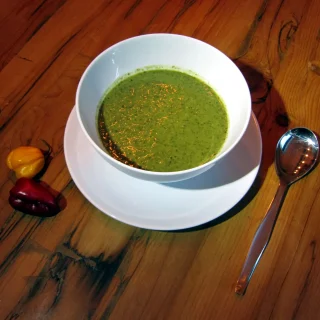 A bowl of smooth green callaloo with hot peppers beside it