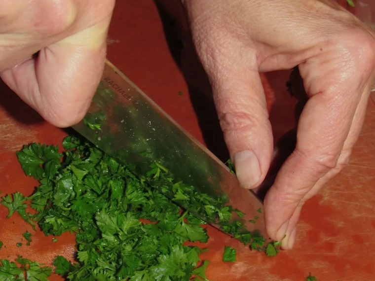 Hands chopping fresh green herbs with a chef's knife