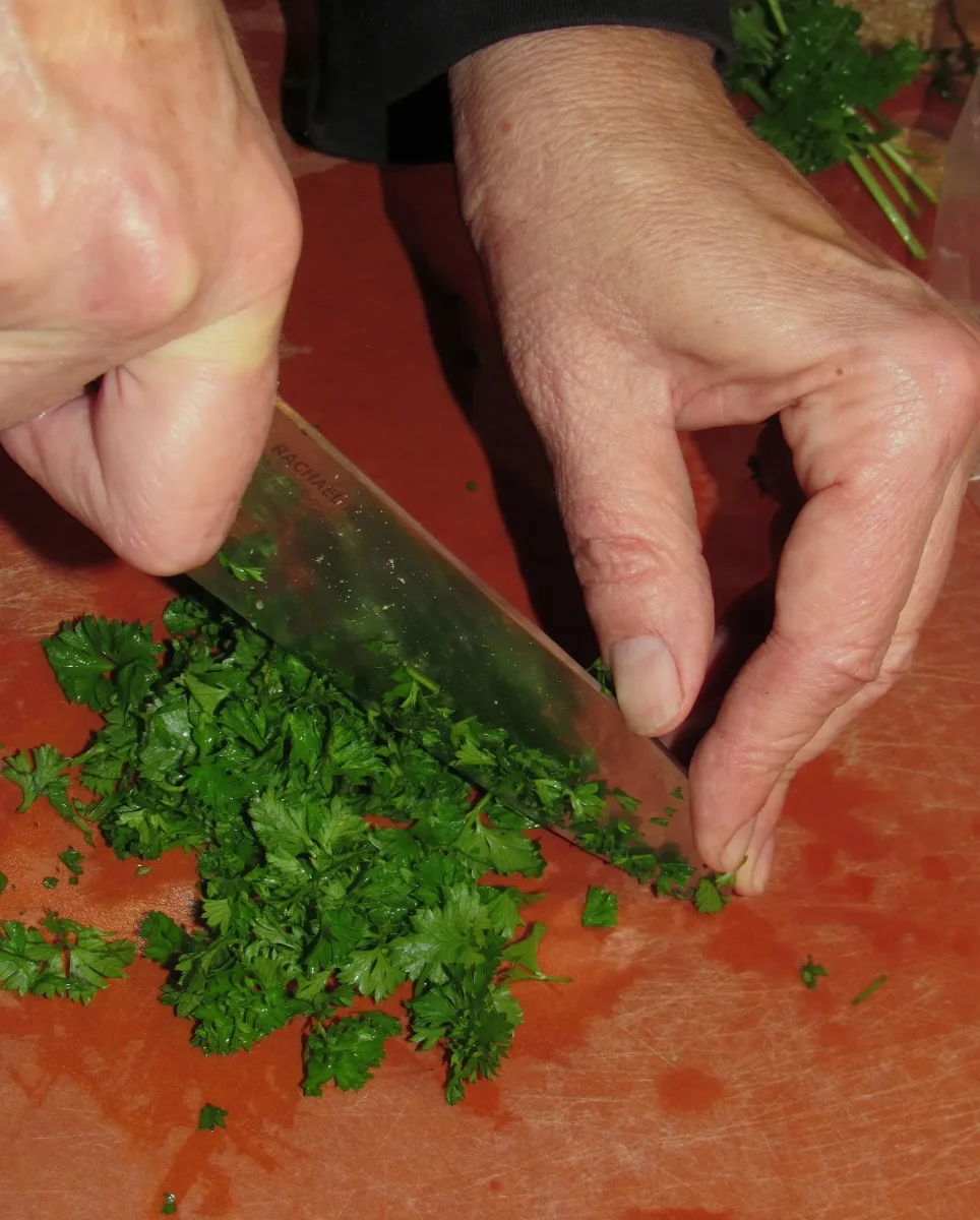 Hands chopping fresh green herbs with a chef's knife