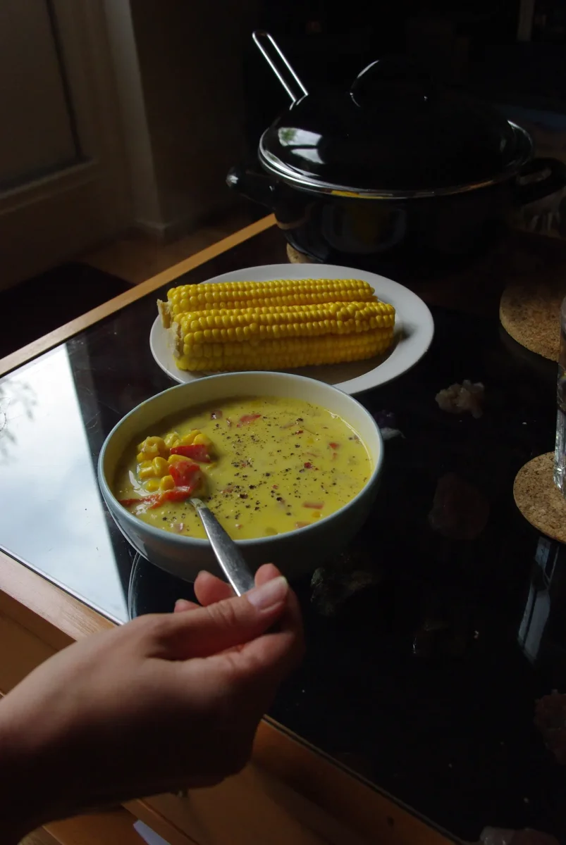 A bowl of corn soup with cobs of corn on a plate behind it