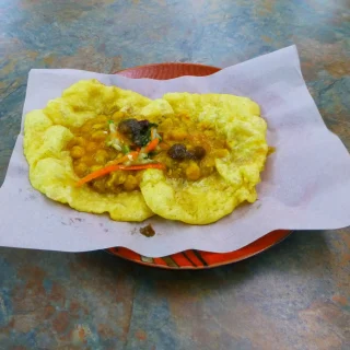 Doubles: two soft yellow bara topped with curried channa, served on paper