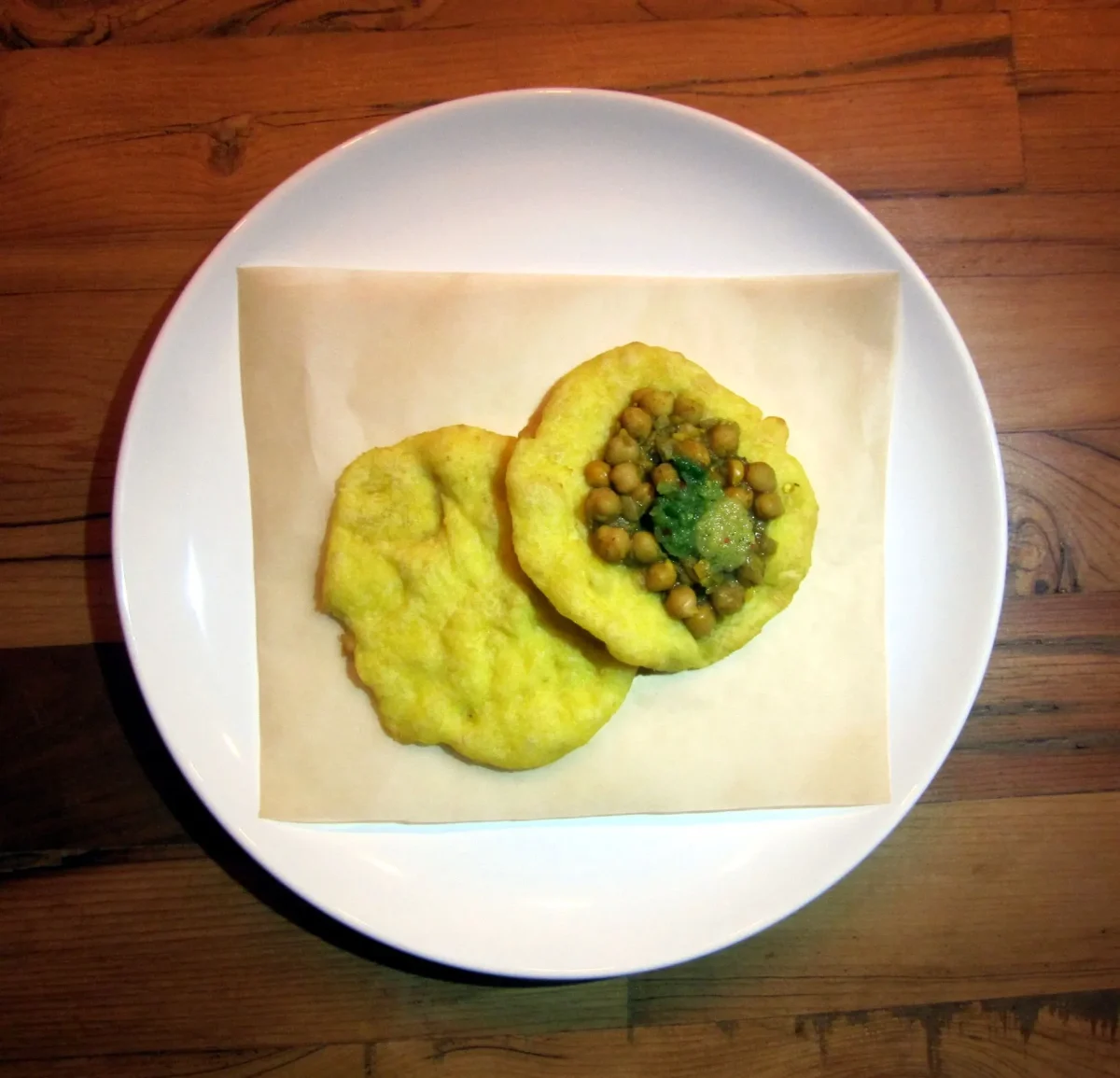 Two bara with curried chickpeas on a white plate