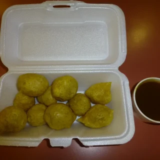 Pholourie in a takeaway box with a cup of dipping sauce