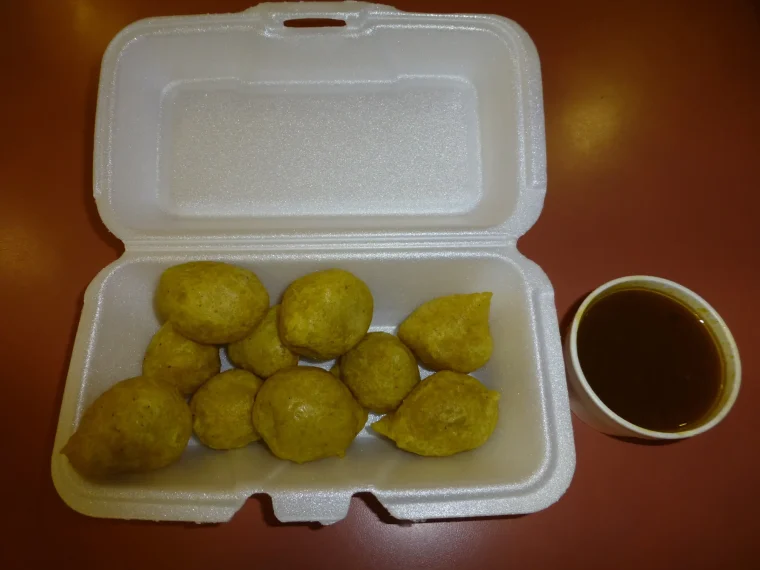 Pholourie in a takeaway box with a cup of dipping sauce