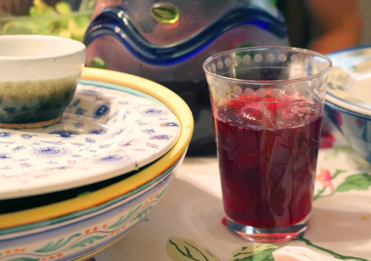 A glass of deep red hibiscus (sorrel) drink on a set table