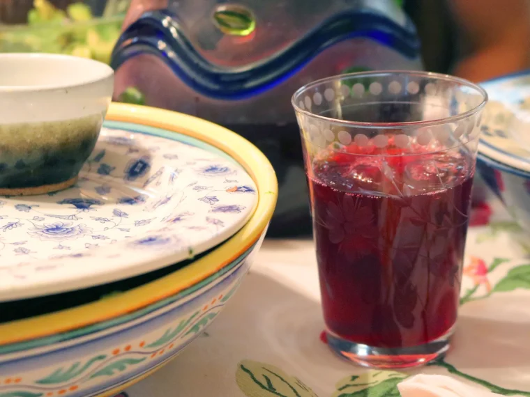 A glass of deep red hibiscus (sorrel) drink on a set table